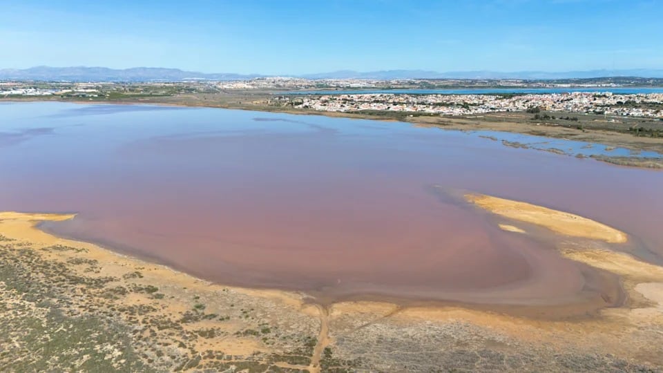 A Pink Salt Lagoon Stretches Across A Dry Landscape